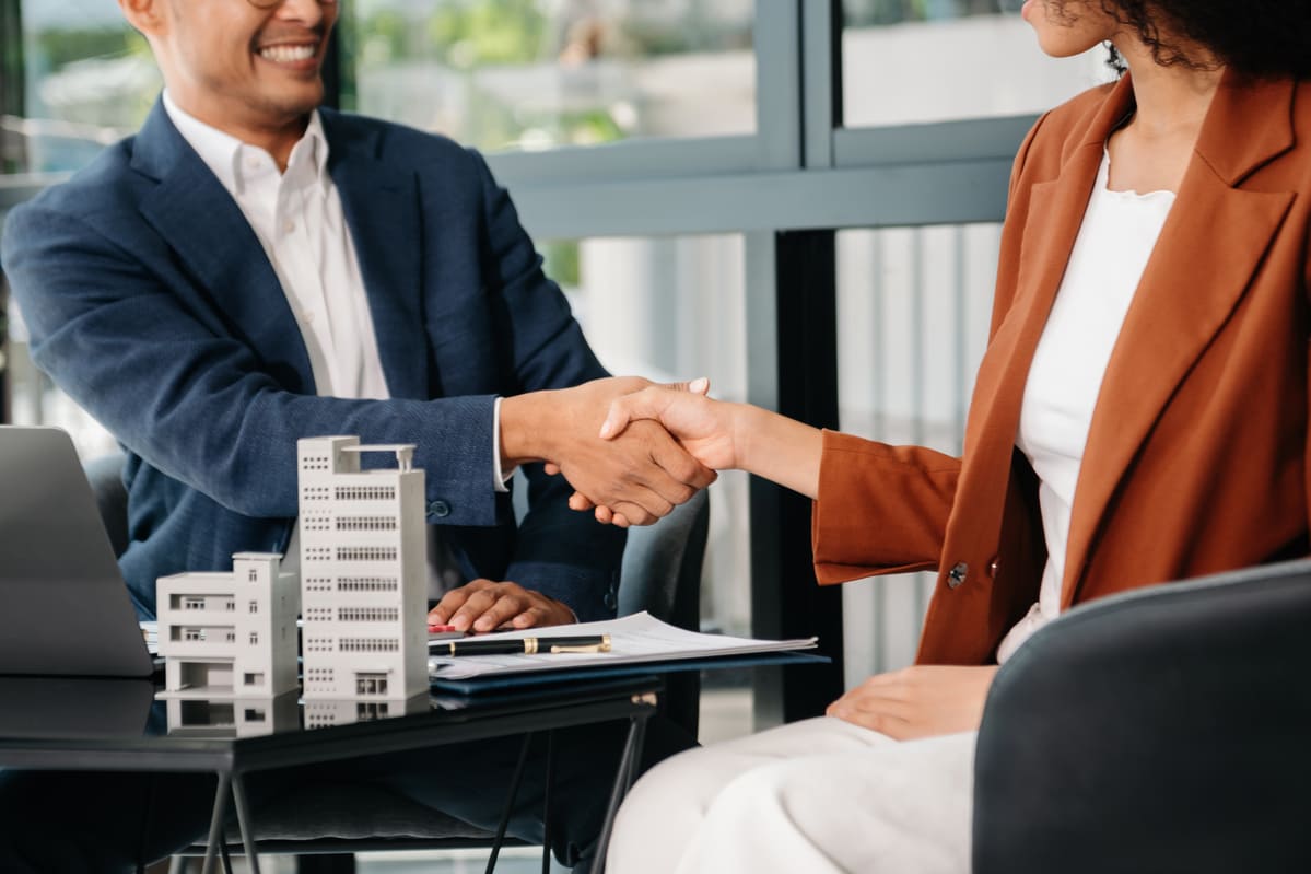 Two professionals shaking hands next to building models.