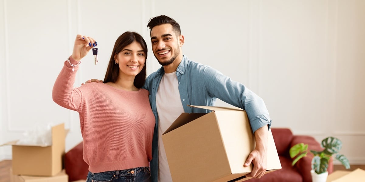 A couple holding keys and boxes moving into a new home